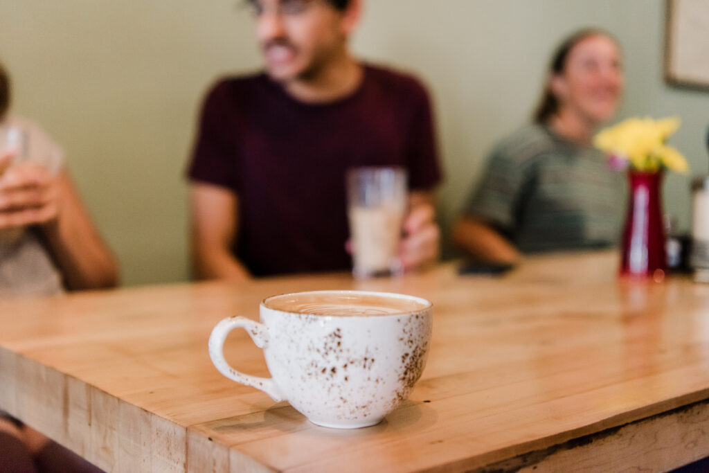 Close-up of a mug full of creamy latte with students sitting in the background.
