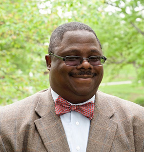 Portrait of Tyson King-Meadows, wearing a suit and bowtie, smiling outside.
