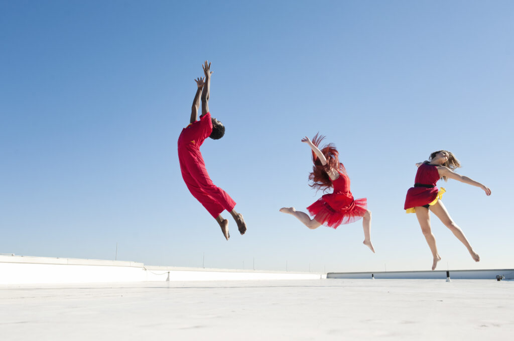 Three dancers leap into the air, looking skyward.
