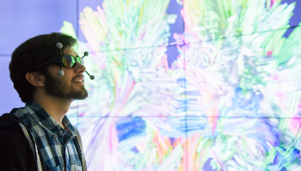 Young man wears VR glasses, standing in front of a glowing wall.