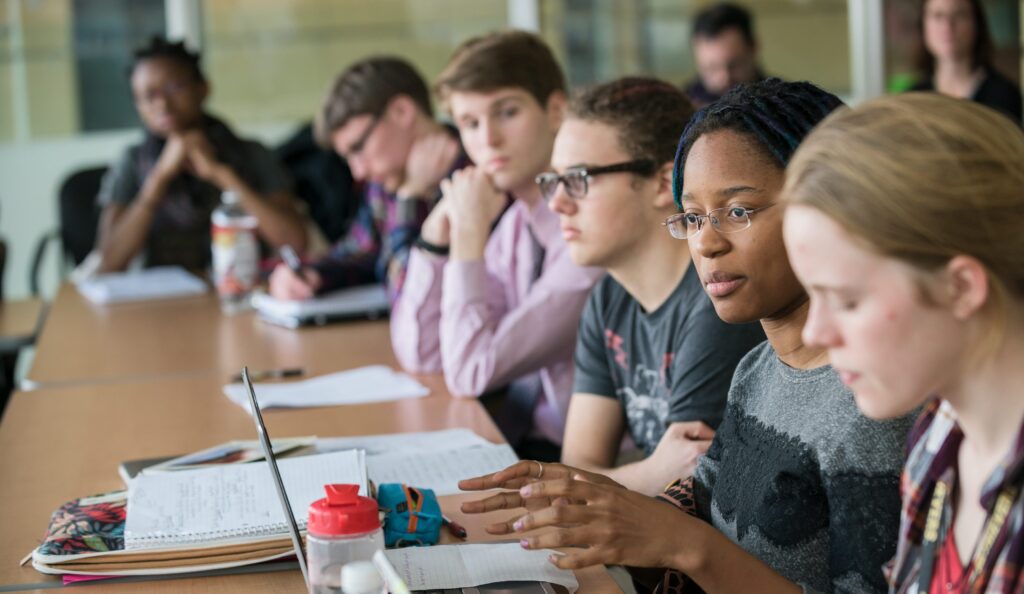 Students sit around a conference table, with one speaking.