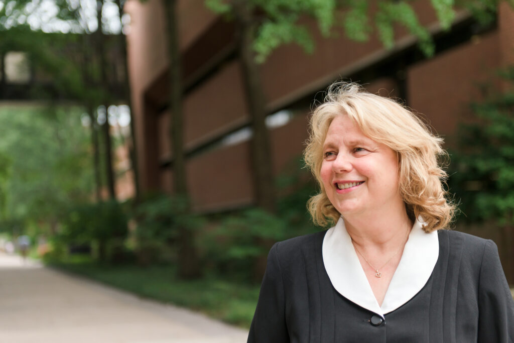 Katharine Cole stands in UMBC's academic row, in front of brick buildings and foliage.