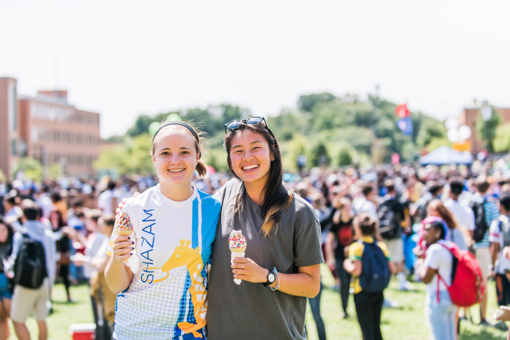 Two UMBC students pose together with ice cream cones in front of a large crowd.