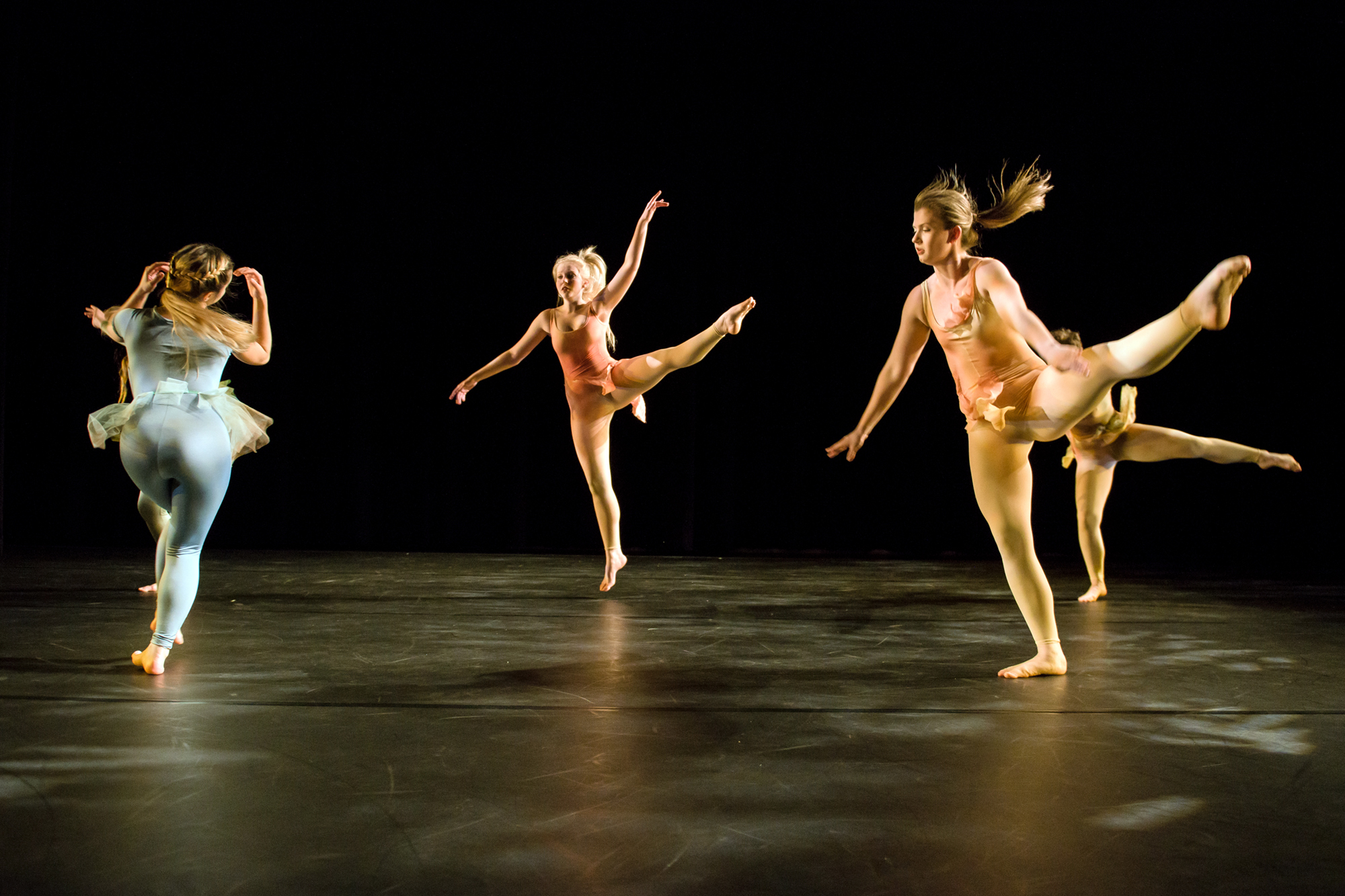 Five dancers on stage against a dark background