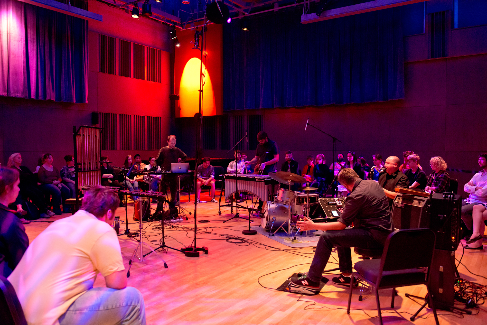 Musicians perform on percussion instruments in a large room bathed with red light