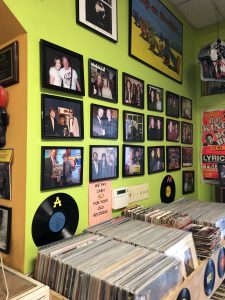 A bright yellow-green wall covered with framed portraits of people, with a shelf full of boxes of vinyl records sitting in front.