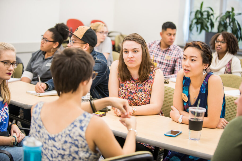 Several college students gather around a table, in conversation