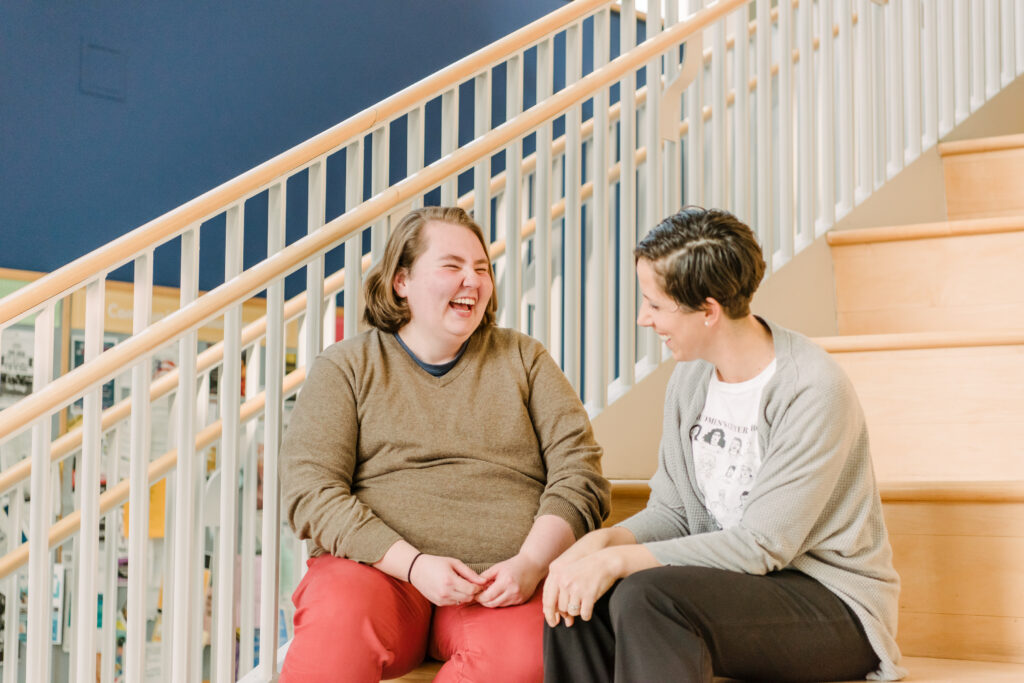 Two people sit, talking and smiling, on steps in the UMBC Commons.