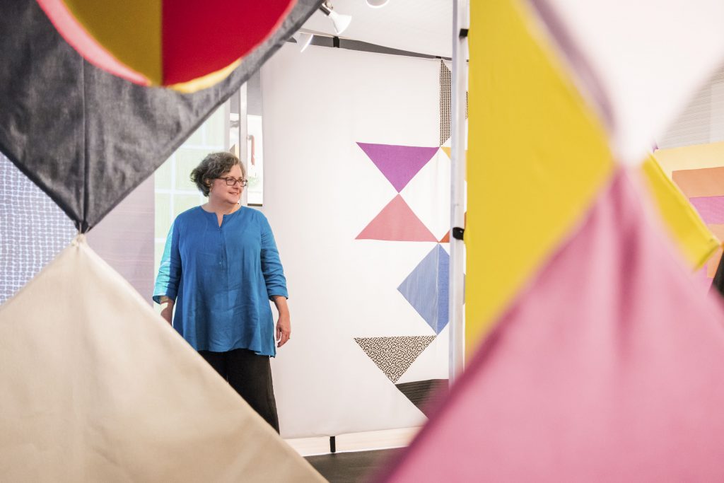 Margaret Re standing in her colorful textile installation.