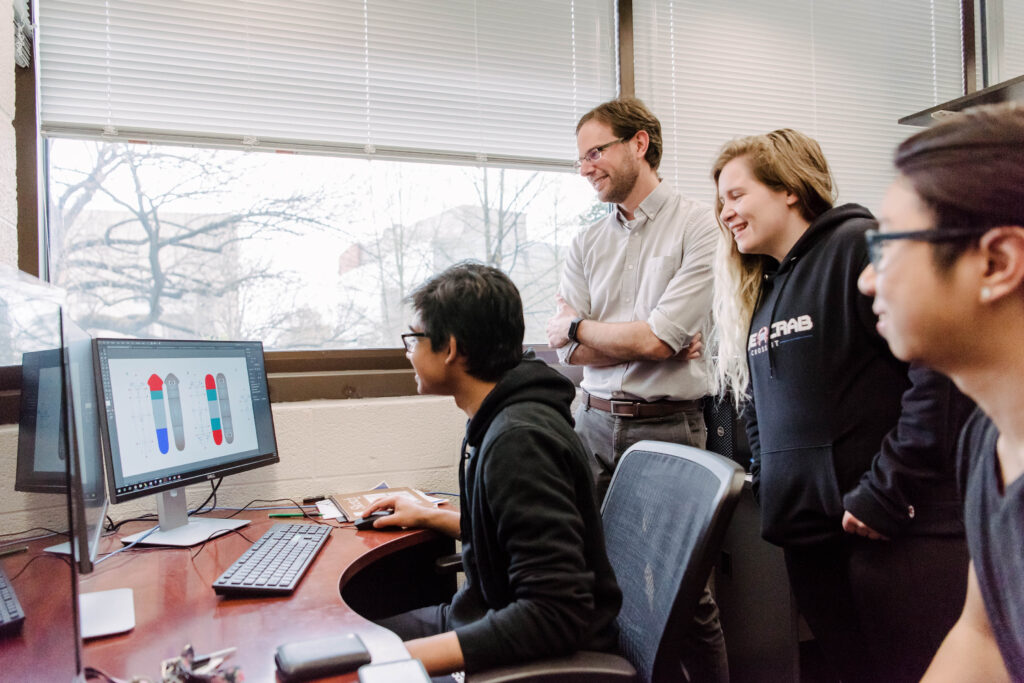 Faculty member and three students gathered around a computer showing figures of planaria worms.