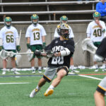 Men's lacrosse player in action on the field, as players from the opposing team stand in the background.