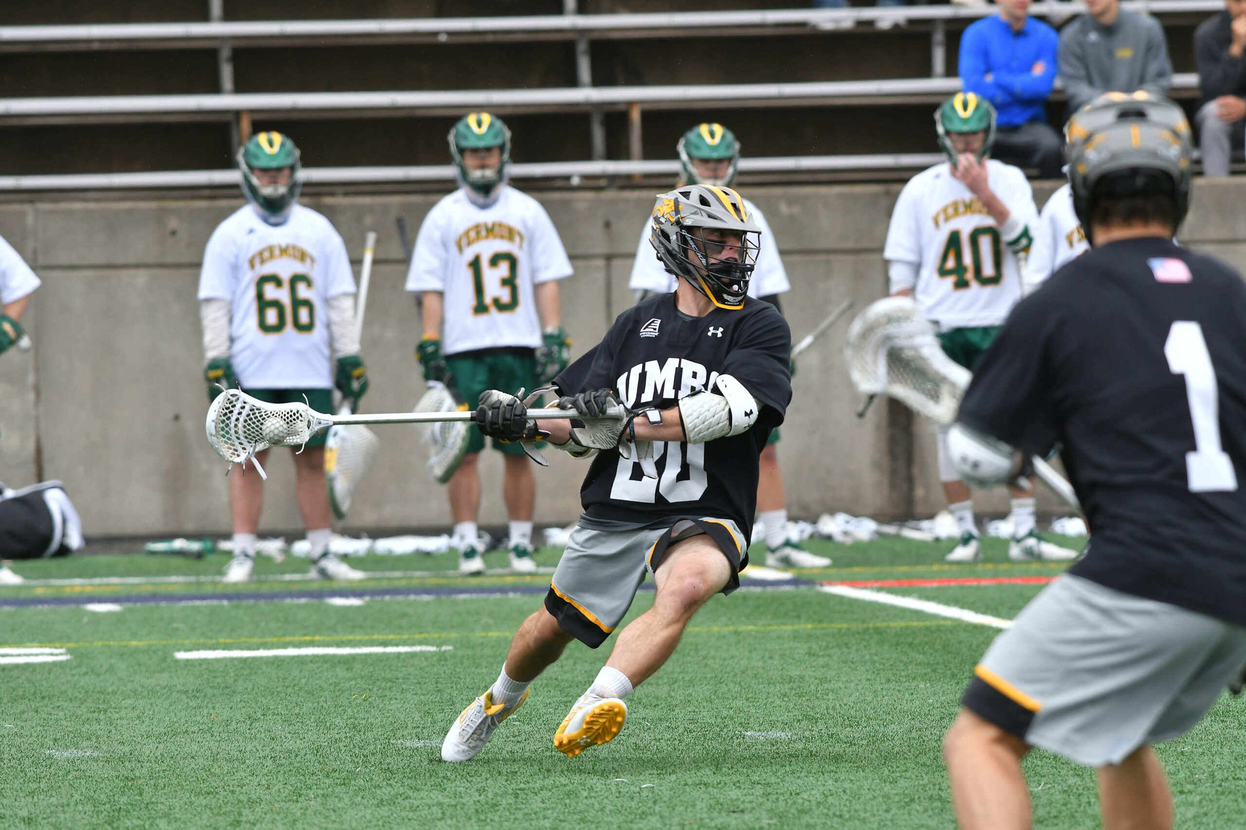 Men's lacrosse player in action on the field, as players from the opposing team stand in the background.