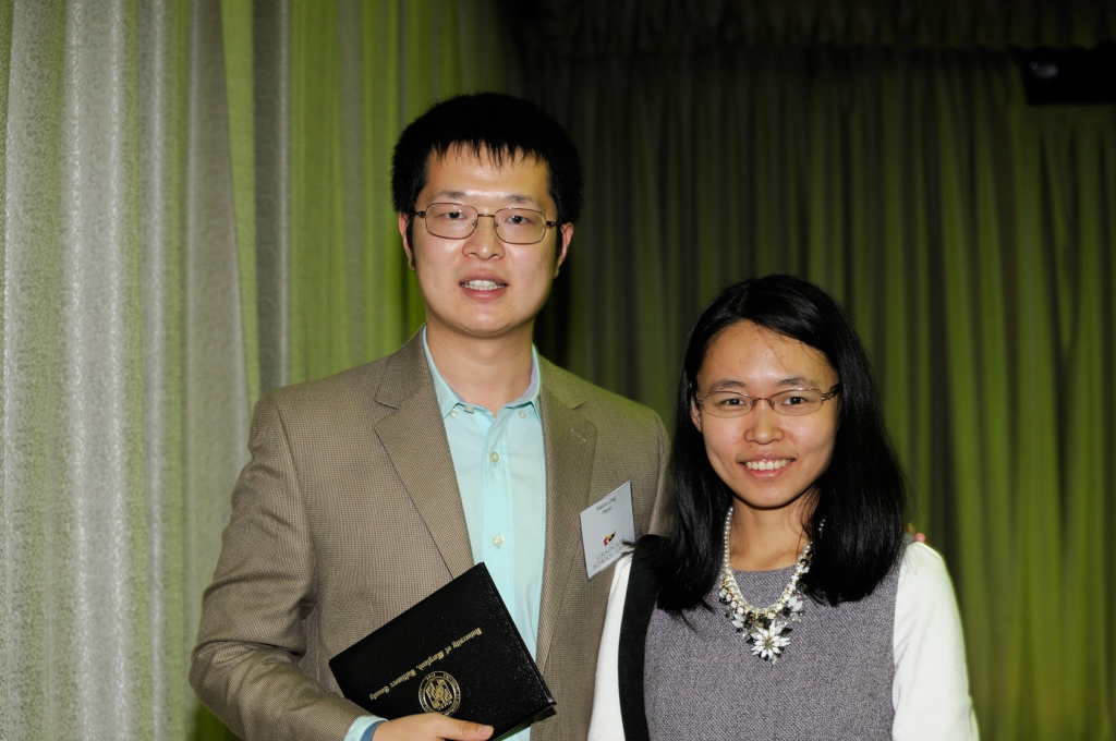 A man and woman stand next to each other, in front of a curtain in a ballroom.