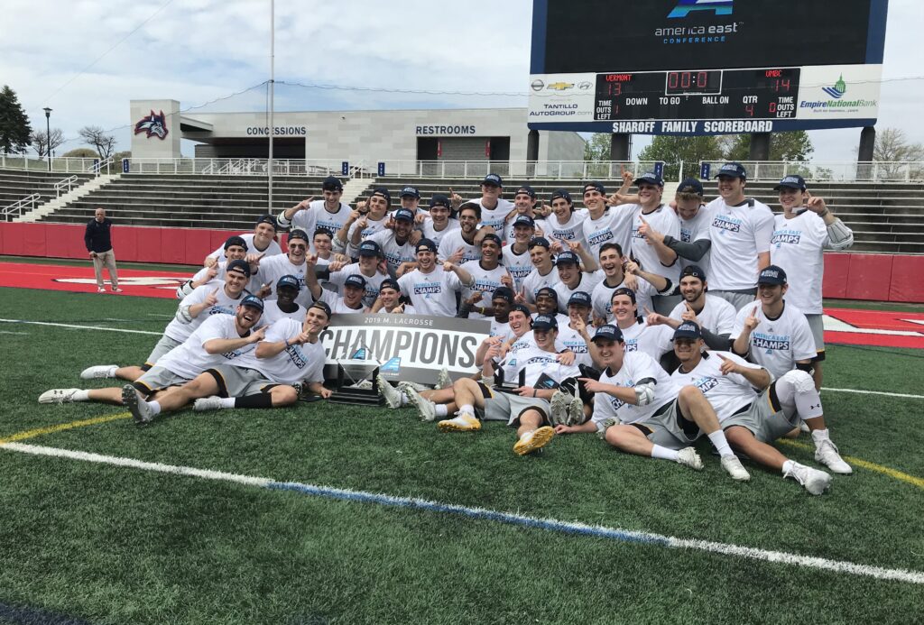 UMBC Men's Lacrosse team poses with America East Championship banner on the field