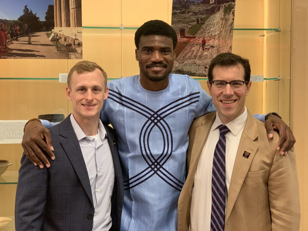 A student poses with two staff members, all three smiling, inside an arts building.