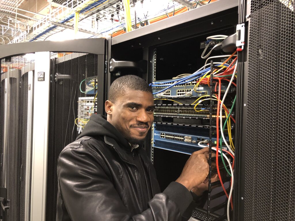 Man stands in front of powerful computing equipment, moving cables.