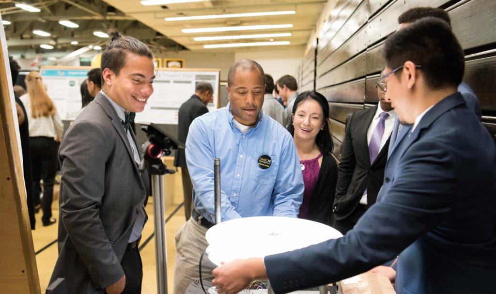 People in professional clothing gather around an electronic device.