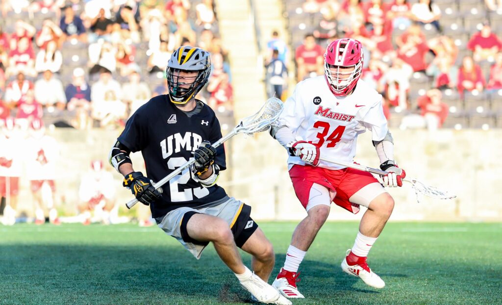 UMBC lacrosse player in black, gold and gray uniform and Marist lacrosse player in red and white uniform, on the field.