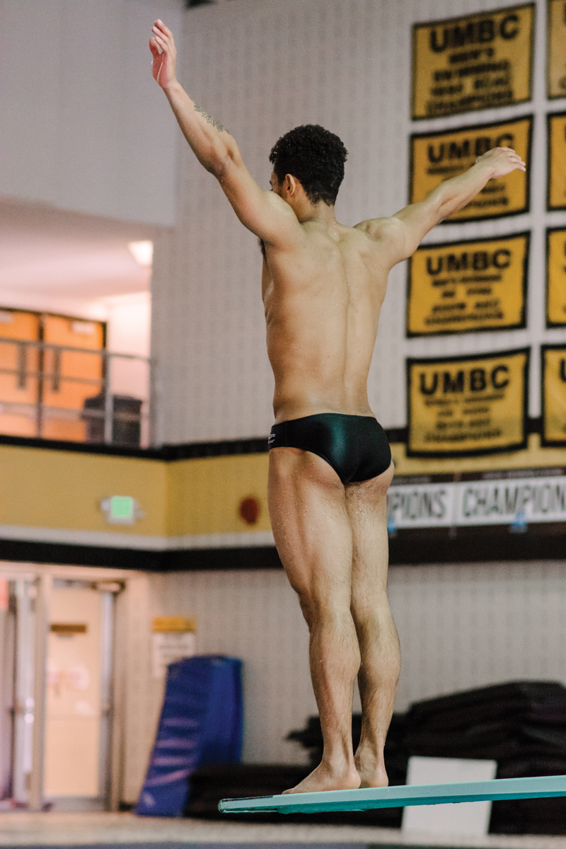 diver stands on diving board arms extended