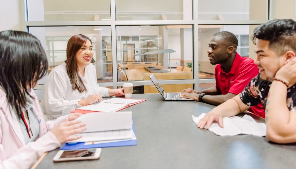 A diverse group of students sitting at a table together, talking and studying.