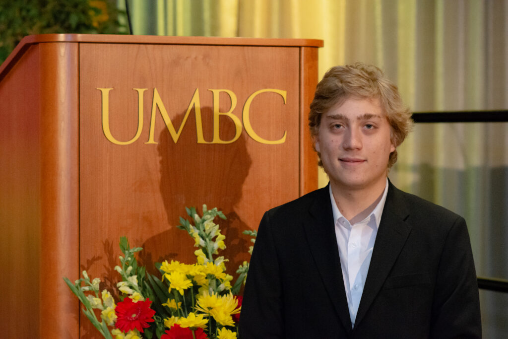 Young man with blonde hair stands in front of podium reading 