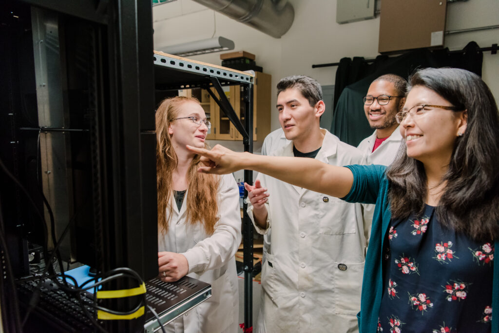 Professor (at right) points to results on a screen, while a group of students looks at them and discusses.