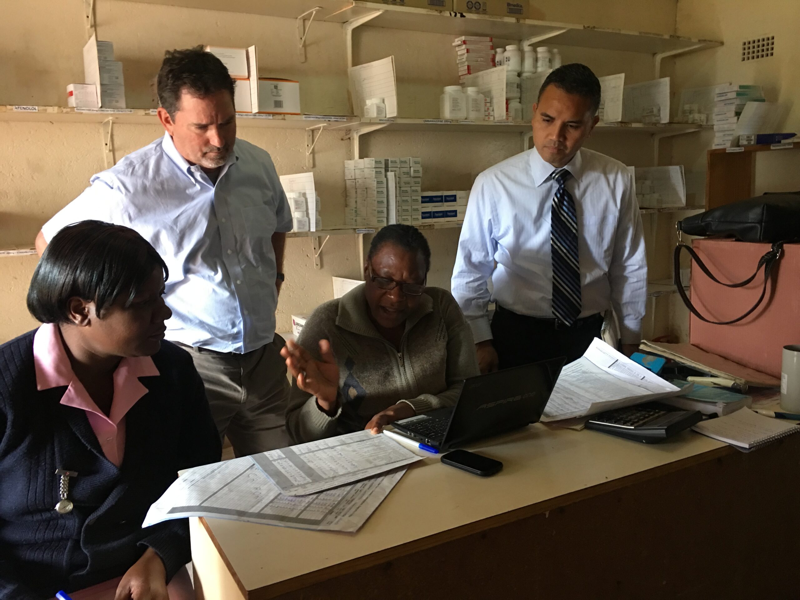 Shelsby, standing on the left, visits a pharmacy in Zimbabwe as the manager shows him how she keeps her inventory records. Photo courtesy of Shelsby.
