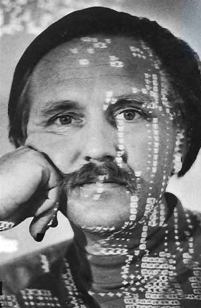 In a black and white image, a man with a mustache looks at the camera. A pattern of lights is projected onto his face.