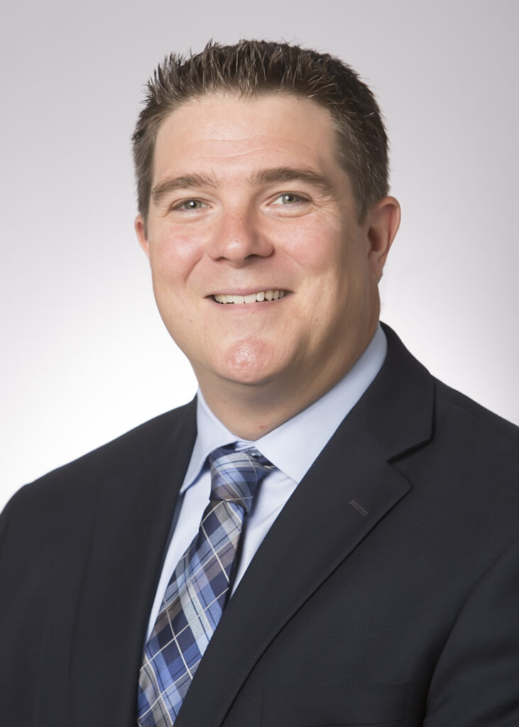 Headshot of middle-aged man, smiling, in jacket and tie.