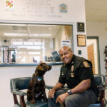 Sergeant Cheatem smiles at the camera as UMBC Police comfort dog looks at him