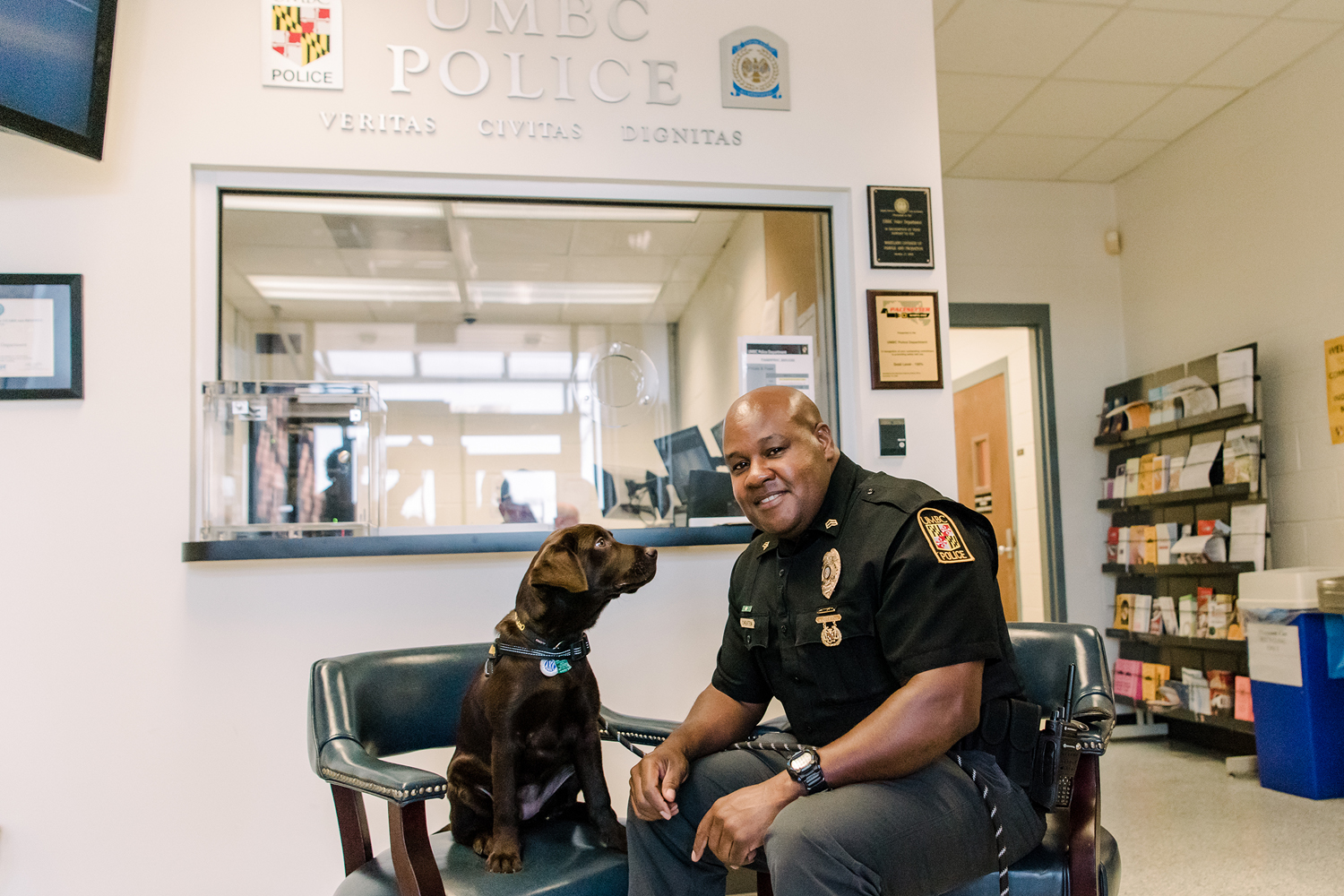 Sergeant Cheatem smiles at the camera as UMBC Police comfort dog looks at him