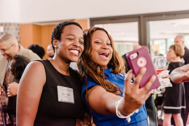Two black women dressed nicely taking a selfie together on an iPhone.