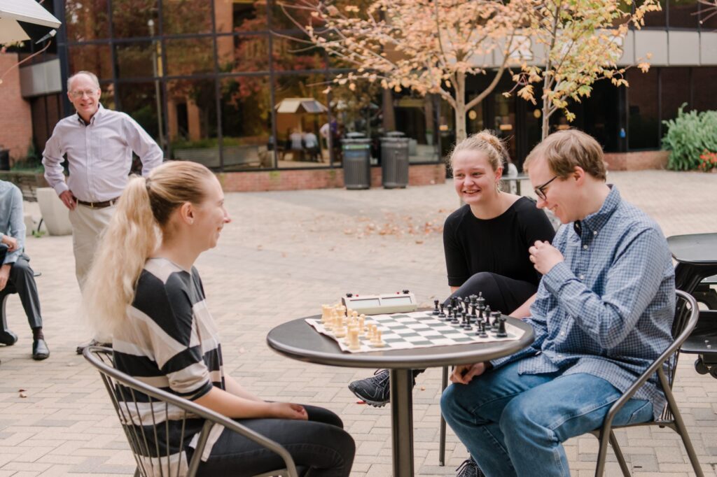 Three UMBC students play chess outside.