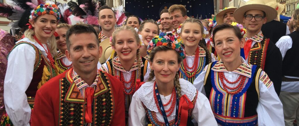Large group of men and women dressed in traditional Polish clothing standing together at an outdoor Polish folk festival in Poland.