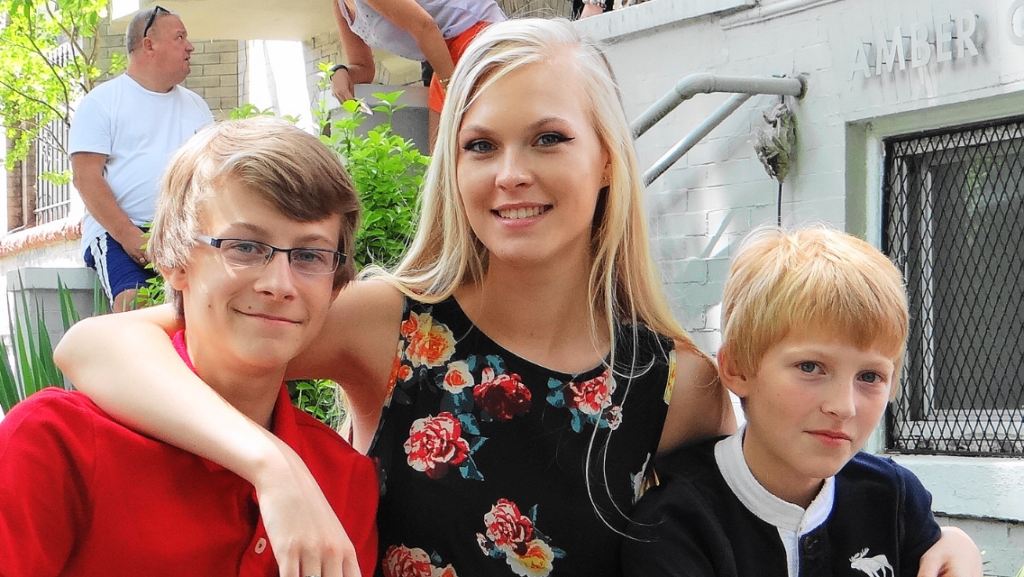 A teenage girl stand between her two younger brothers.