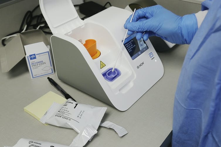 A lab technician using a swab to put a sample into a rapid test machine.