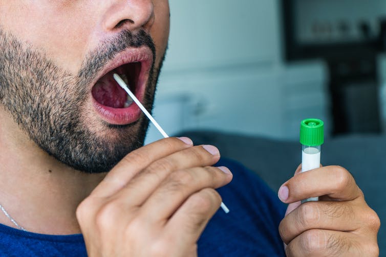 A man inserting a swab into his mouth while holding tube to contain the sample.