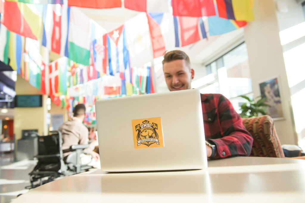 Man works on computer in a room filled with flags. His laptop has a sticker with a Retriever and 