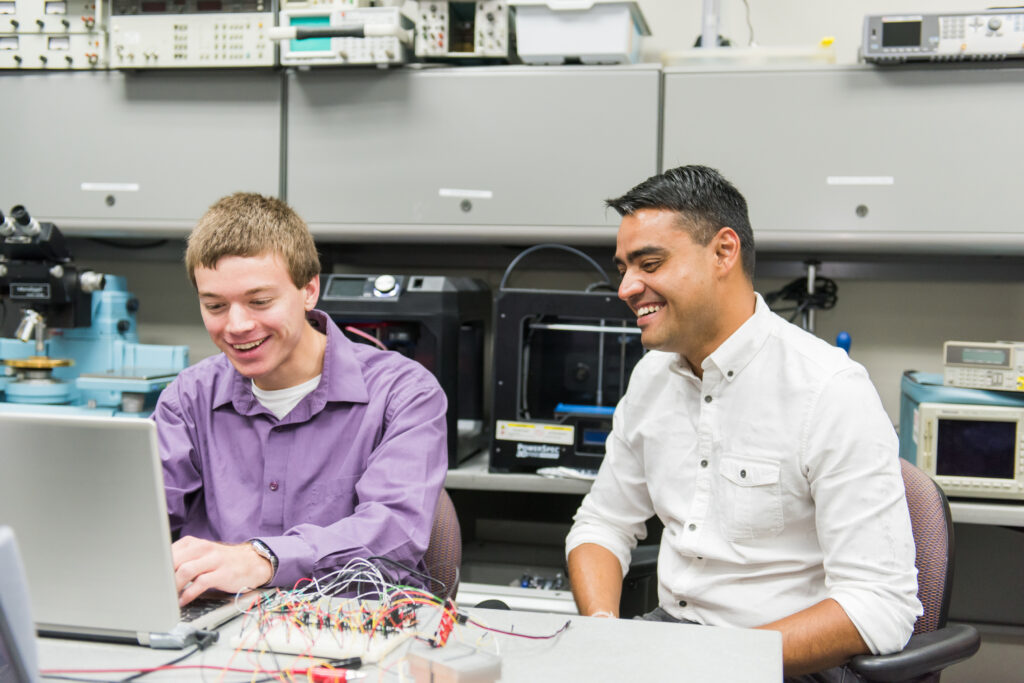 A student and professor work in an engineering lab, seated in front of a computer.