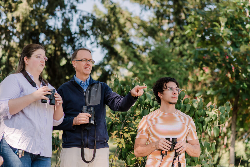 three people outdoors with binoculars