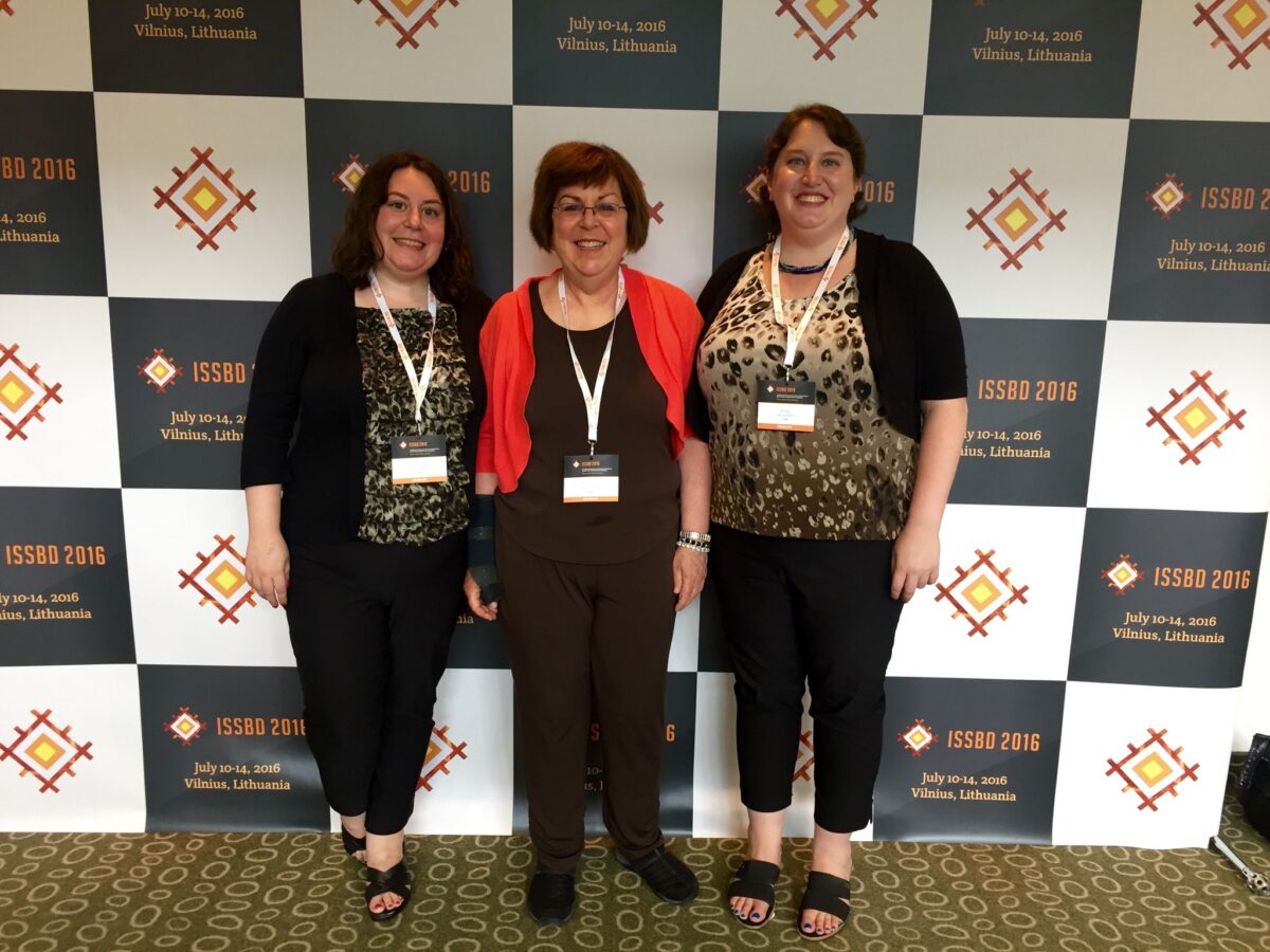 Two adult daughters flank their mother in front of a conference wall