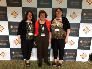 Two adult daughters flank their mother in front of a conference wall