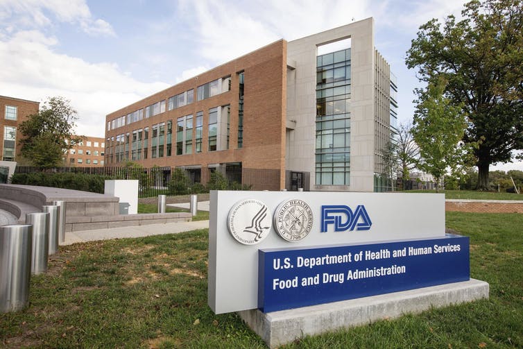 A sign showing the FDA logo with the FDA headquarters in the background.