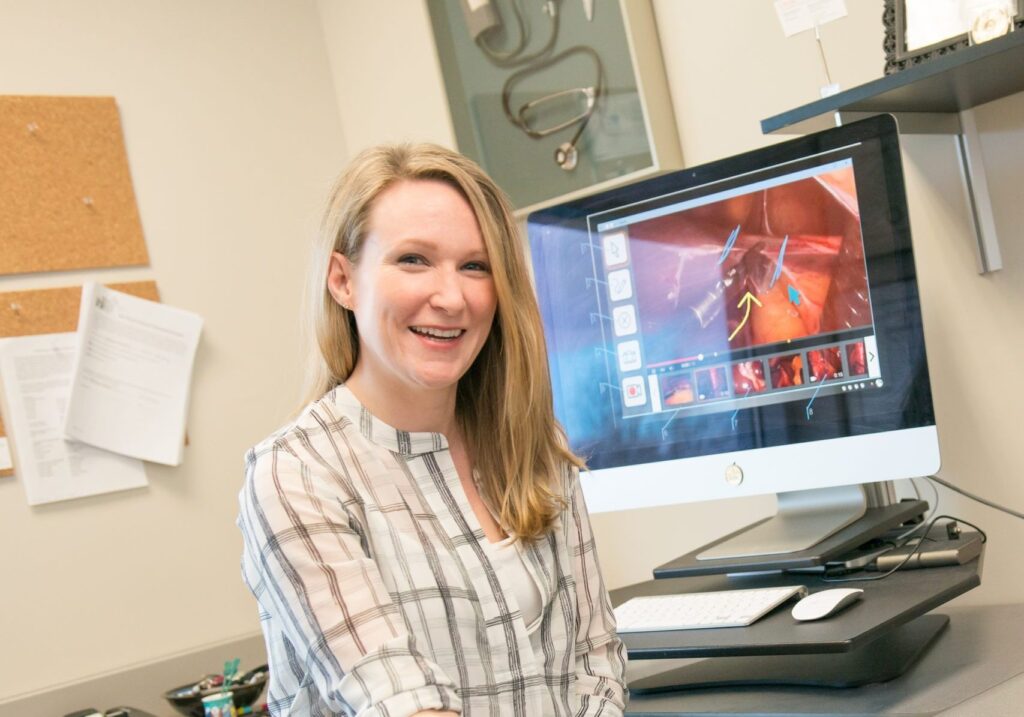 Portrait of smiling woman sitting in front of computer that features medical device imagery.