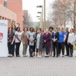 Fifteen women stand in a group together next to a white standup banner with the words Maryland Early Childhood Leadership Program. There are brick buildings next and behind them.