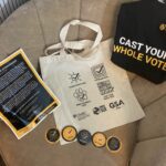 T-shirt, canvas bag, flyer and stickers with large text reading, "Cast Your Whole Vote"