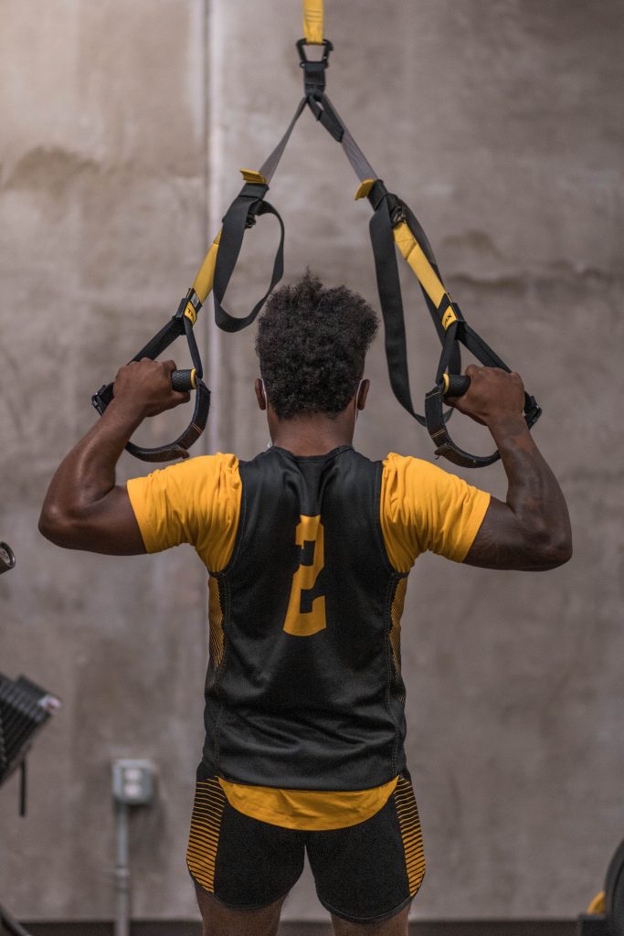 Men's basketball player wearing number 2 on jersey uses exercise equipment to strengthen arms.