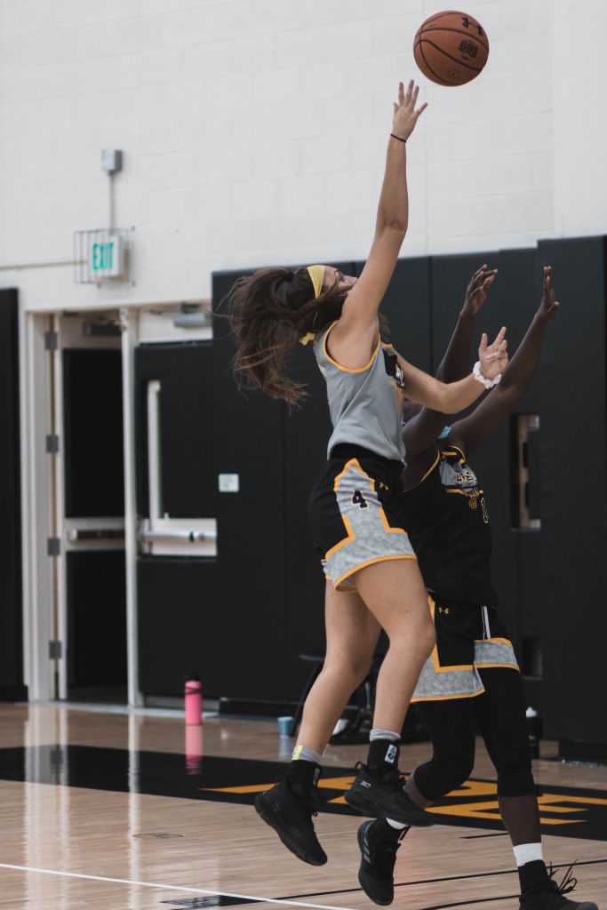 Two women wearing UMBC sportswear, jumping up and reaching for a basketball.