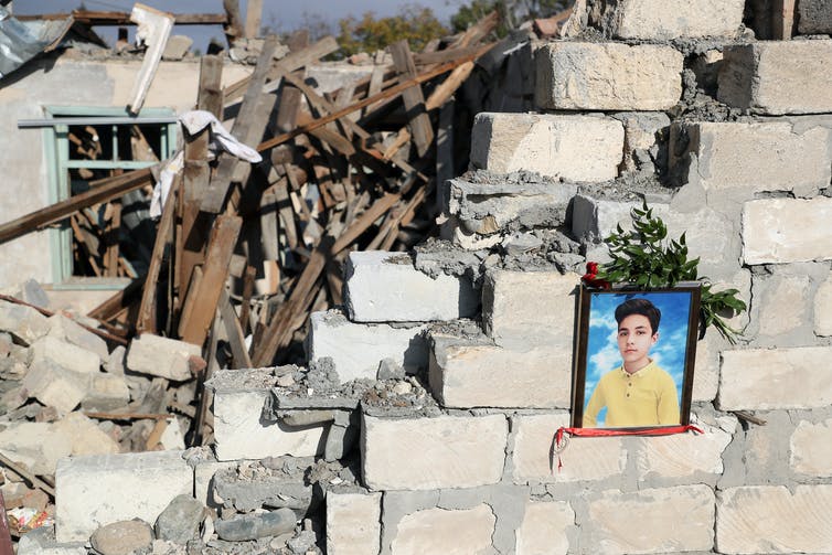 Rubble of a cement home and photo of a boy with flowers around it