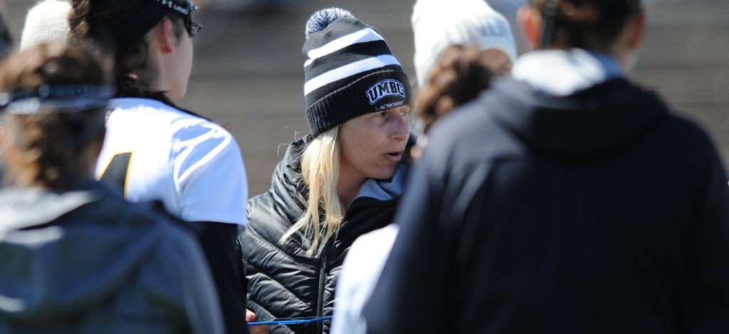 Amy Slade in a winter UMBC hat surrounded by women's lacrosse players.